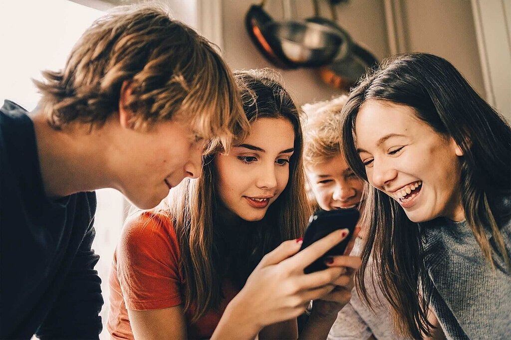 Vier Jugendliche dicht zusammen, eine davon mit Smartphone in der Hand.