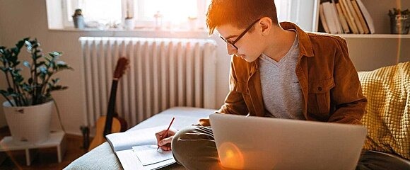 Junge mit Laptop und Heft auf Sofa