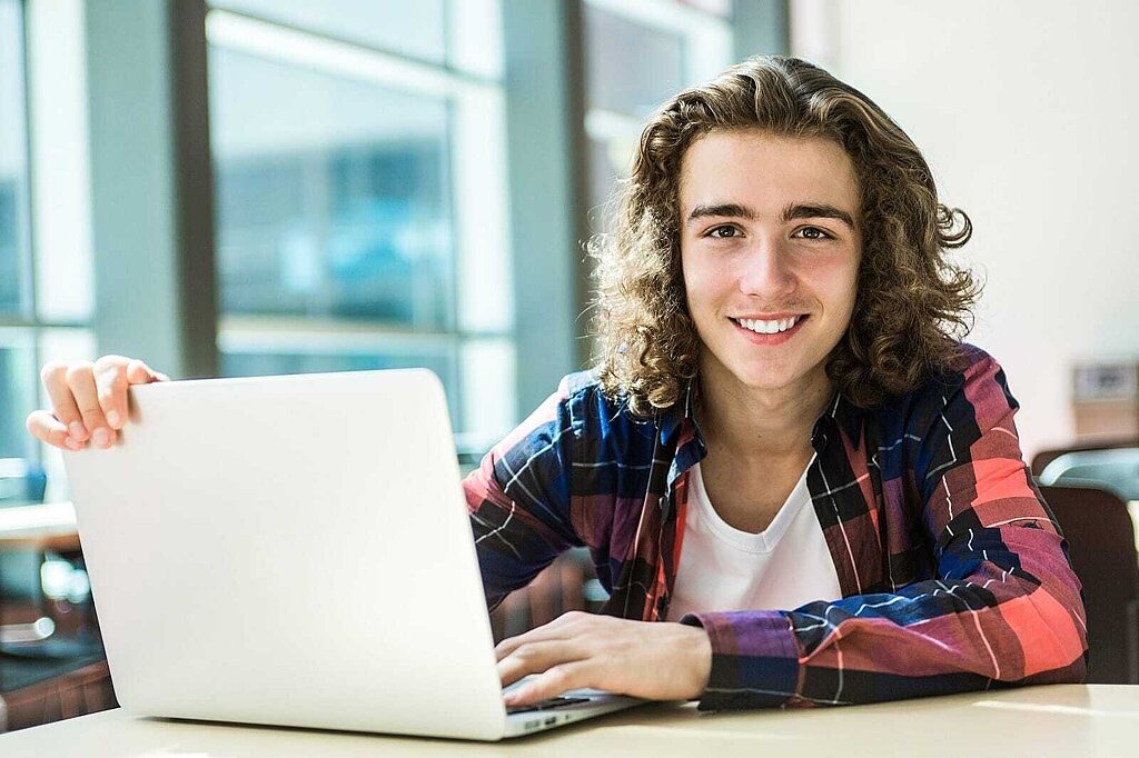 Junge sitzt an einem Tisch mit seinem Laptop.