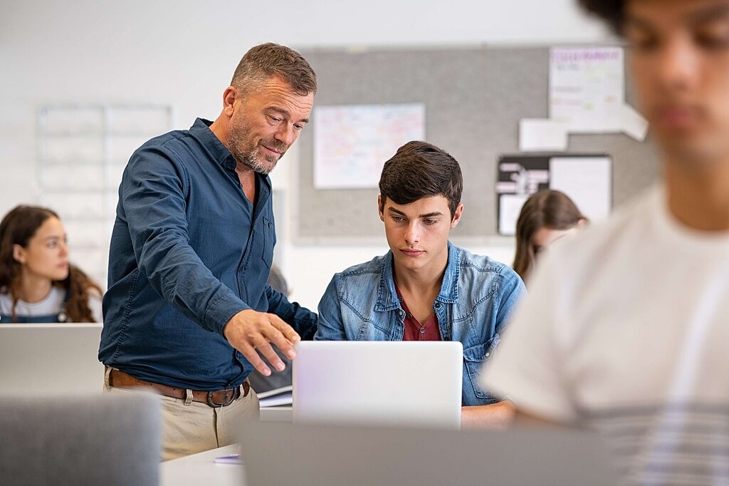 Lehrer erklärt Schülerinnen und Schülern etwas am Computer.